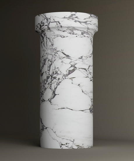 A tall, cylindrical column with a flared top, featuring a smooth surface and a white marble pattern with gray veining, set against a plain, dark background.
