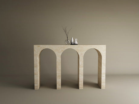 A beige stone console table with three arched openings stands against a plain wall. On top are a glass vase with branches and two ceramic vases in white and gray.