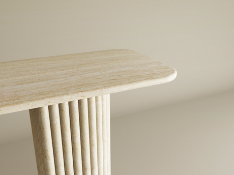 A close-up of a beige stone table with a rounded rectangular top and a fluted cylindrical leg, set against a plain beige background.