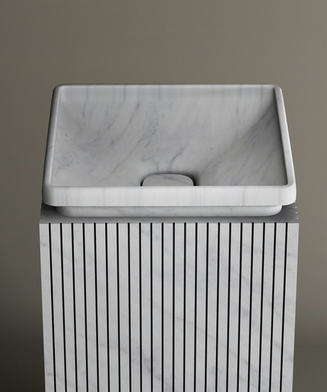A rectangular white marble sink with soft edges sits on a vertically striped marble pedestal against a plain, beige background.