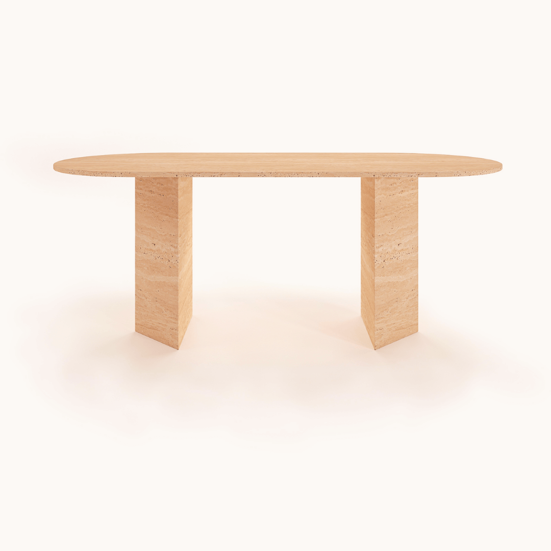 The Grand Pillar Travertine Dining and Meeting Table by Travertable features a minimalist, modern design with an oval top and two rectangular block legs. The tables light, natural finish embodies simplicity and elegance, set against a neutral background.