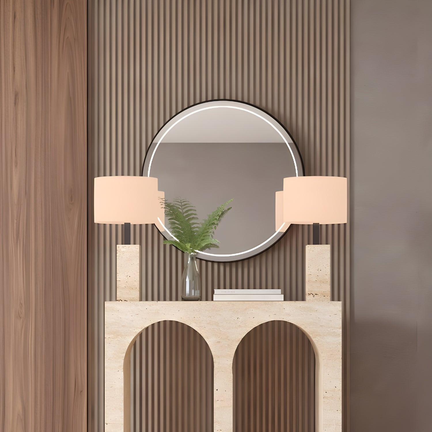 The TRAVERTABLE Travertine Console Table with Two Arches, crafted from solid stone, holds matching lamps, a vase of green ferns, and a closed book. A round mirror on the paneled brown wall completes this modern, sophisticated look.