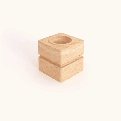 The Travertable Vintage Charm Travertine Vase is a square, beige stone piece with a rough texture and carved layers. It features a circular top depression, suggesting it could be used as a base or holder. The background is plain white.