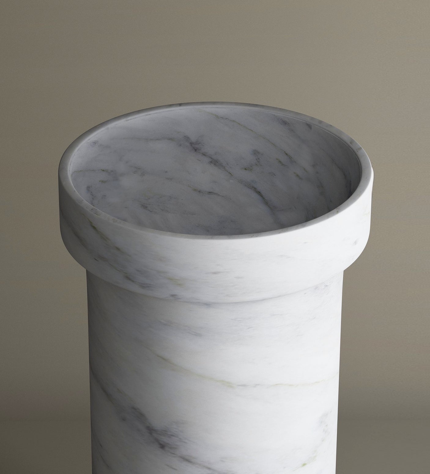 The TRAVERTABLE Carrara Marble Pedestal Vanity Sink, featuring subtle grey veining and a thick, rounded rim, is showcased empty against a plain beige background. Its cylindrical form is viewed from a slightly elevated angle.