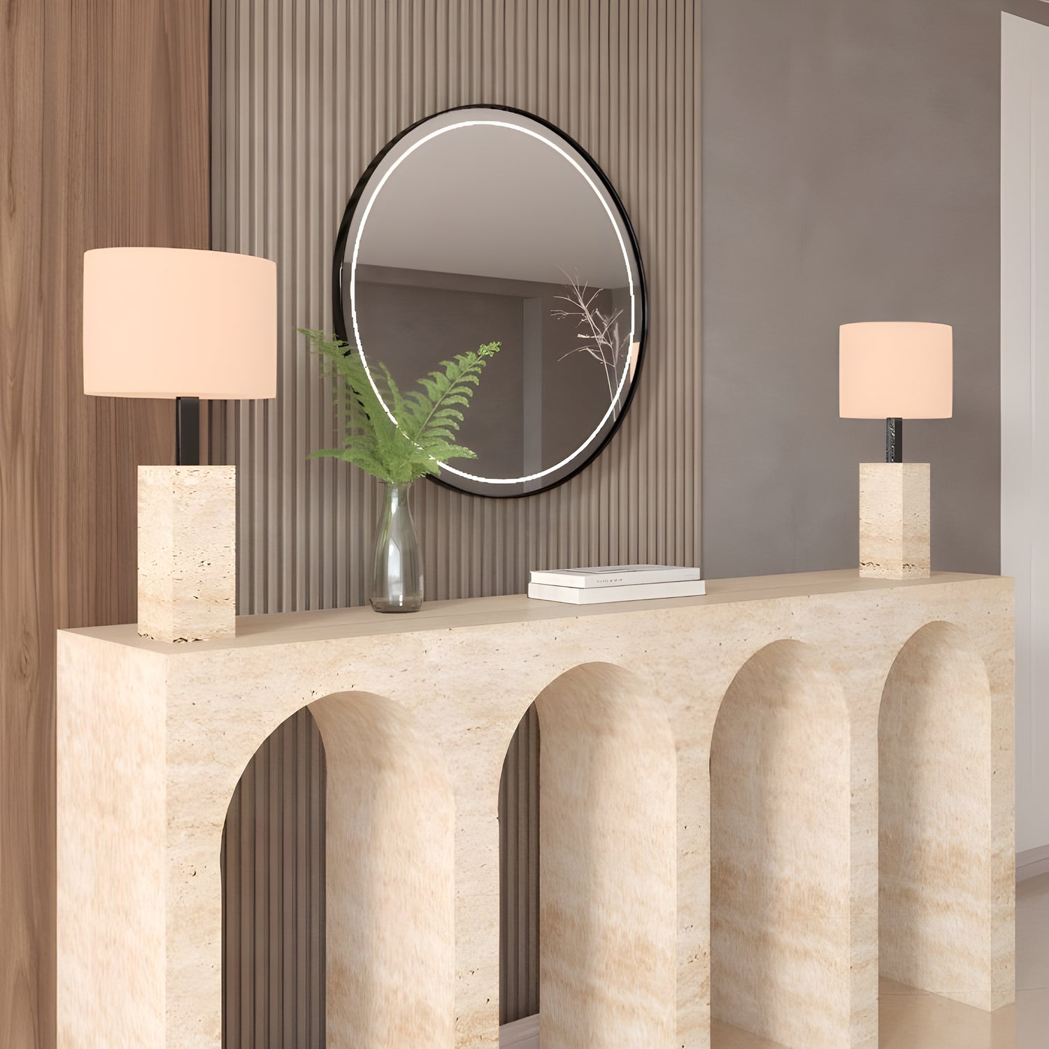 The TRAVERTABLE Travertine Console Table with Four Arches displays two square-based beige lamps, a glass vase with green fern leaves, and a stack of books. A round mirror hangs on the ribbed wall behind this architectural stone console.