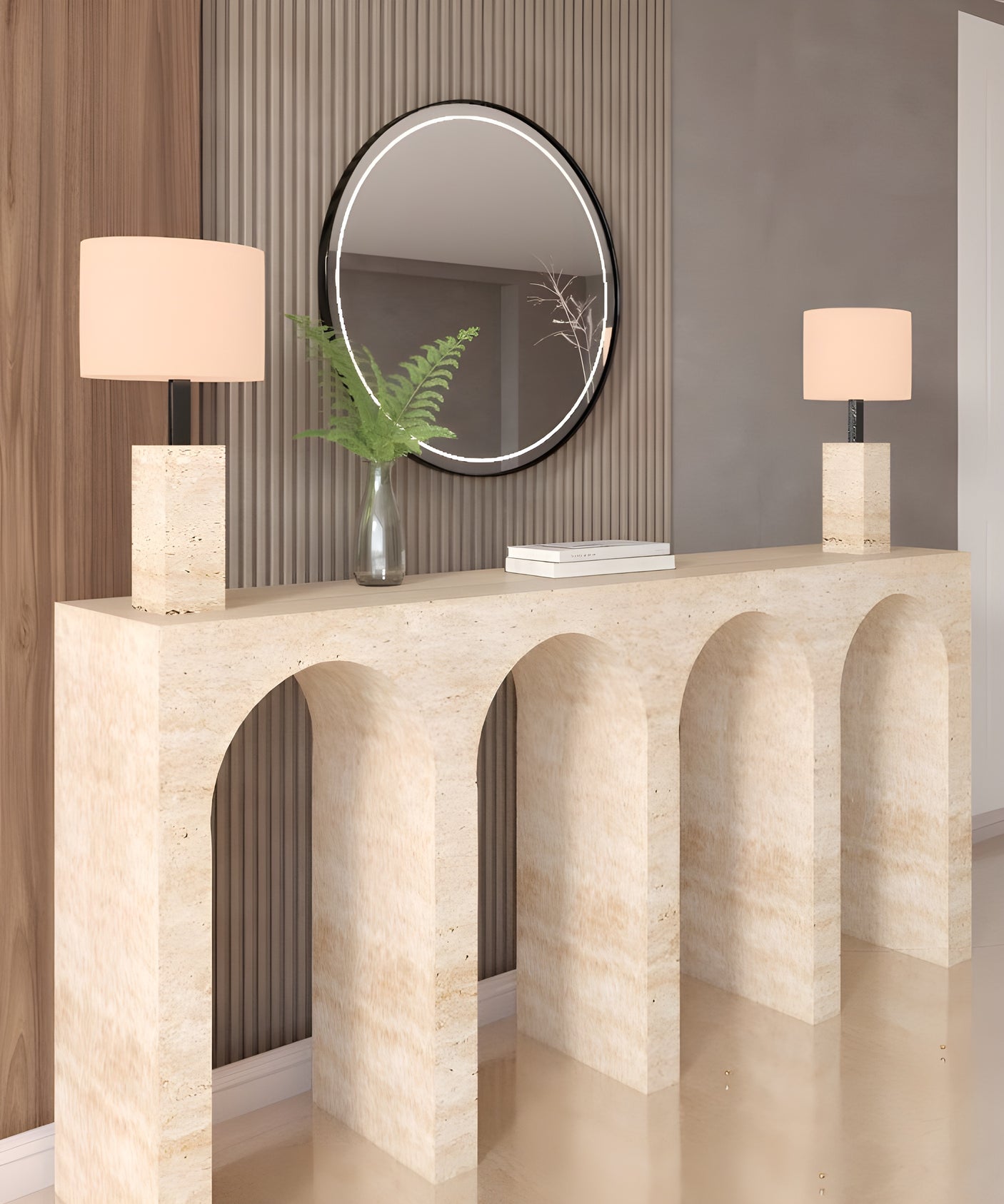 The TRAVERTABLE Travertine Console Table with Four Arches displays two square-based beige lamps, a glass vase with green fern leaves, and a stack of books. A round mirror hangs on the ribbed wall behind this architectural stone console.