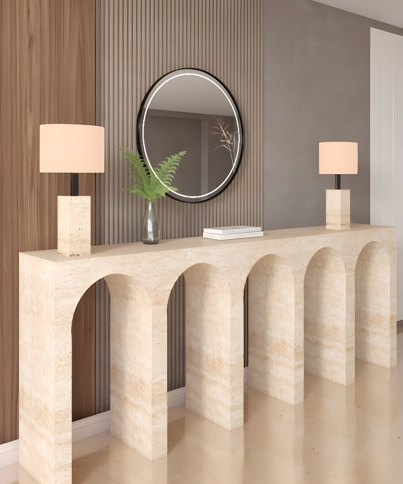 A modern entryway exudes understated luxury with the TRAVERTABLE Travertine Console Table with Five Arches, two white-shaded lamps, a round mirror above, and a glass vase of green fern leaves.