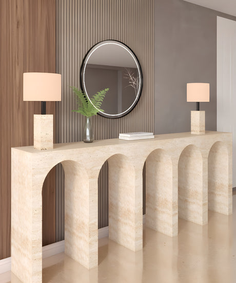 A modern entryway exudes understated luxury with the TRAVERTABLE Travertine Console Table with Five Arches, two white-shaded lamps, a round mirror above, and a glass vase of green fern leaves.