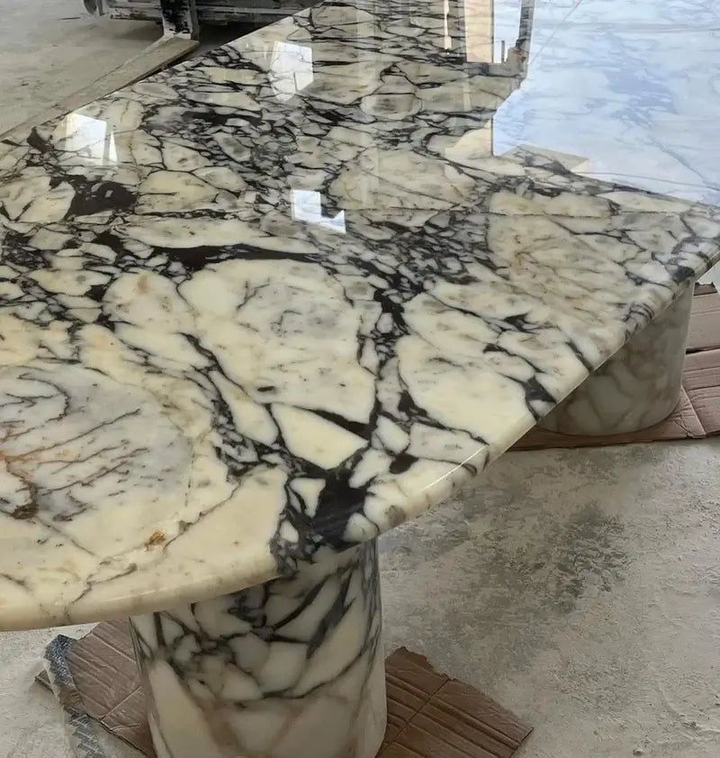 The Arcadia Dining Table by Travertable features a black and white veined marble on two cylindrical pedestals. The polished surface enhances the design, while cardboard pieces on the concrete floor make it customizable into an Eclipse Travertine masterpiece.