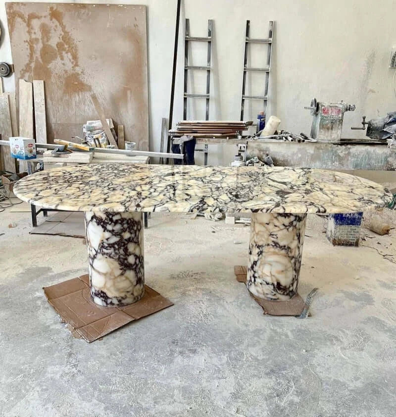 A workshop with the Arcadia Dining Table by Travertable, featuring a uniquely shaped marble travertine top and two cylindrical bases. The rooms ladders, tools, and materials scattered about inspire customization of your table.