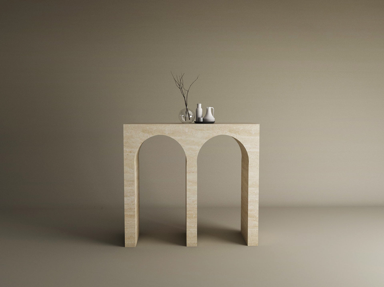 The TRAVERTABLE Travertine Console Table with Two Arches—a solid stone, customizable piece—stands against a taupe backdrop, topped with a clear glass vase of bare branches and two small white ceramic vases.