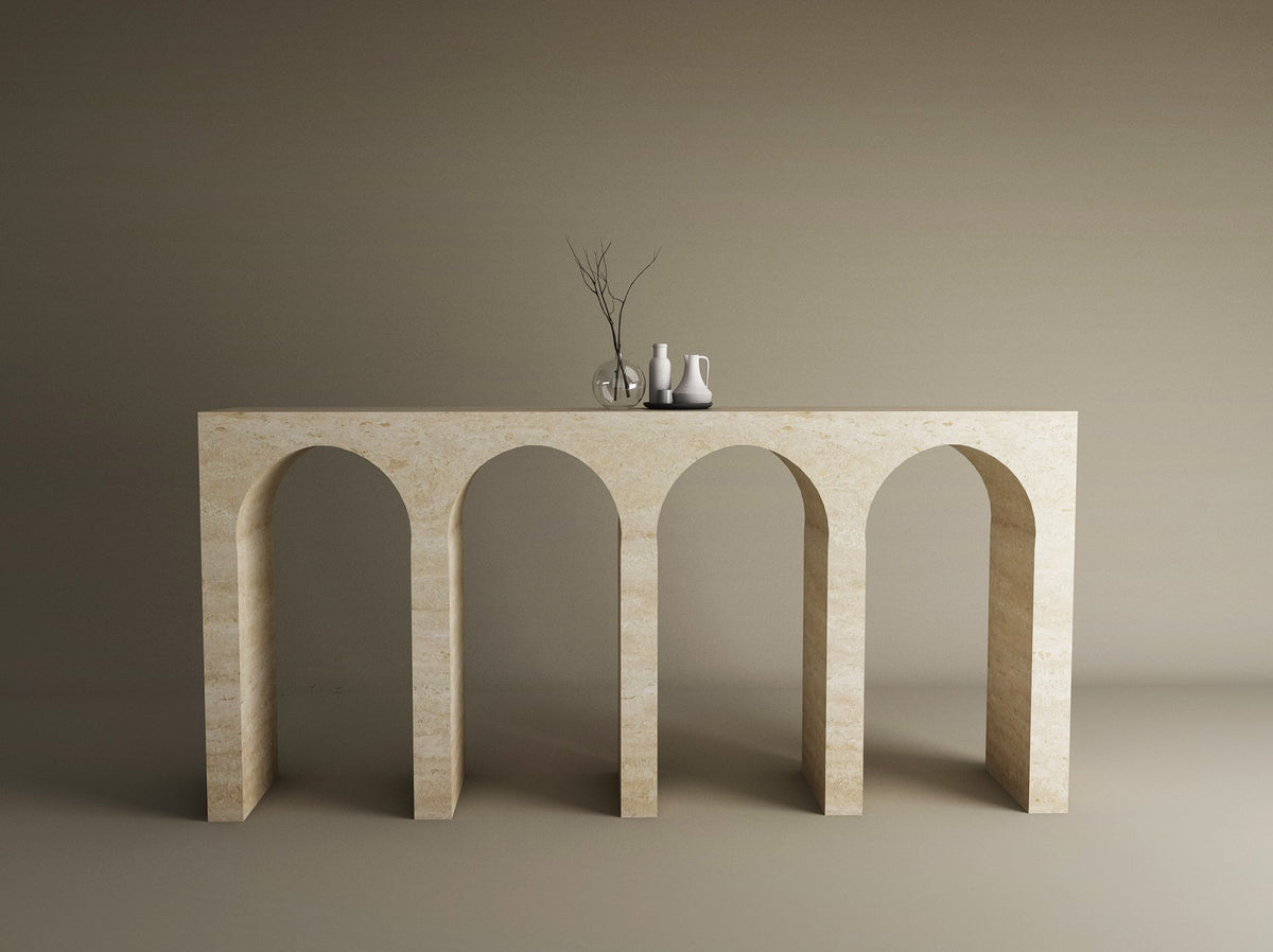 The TRAVERTABLE Travertine Console Table with Four Arches stands against a beige wall, highlighting sculptural elegance. Three minimalist decor pieces on top complete this refined display of the customizable Architectural Stone Console.