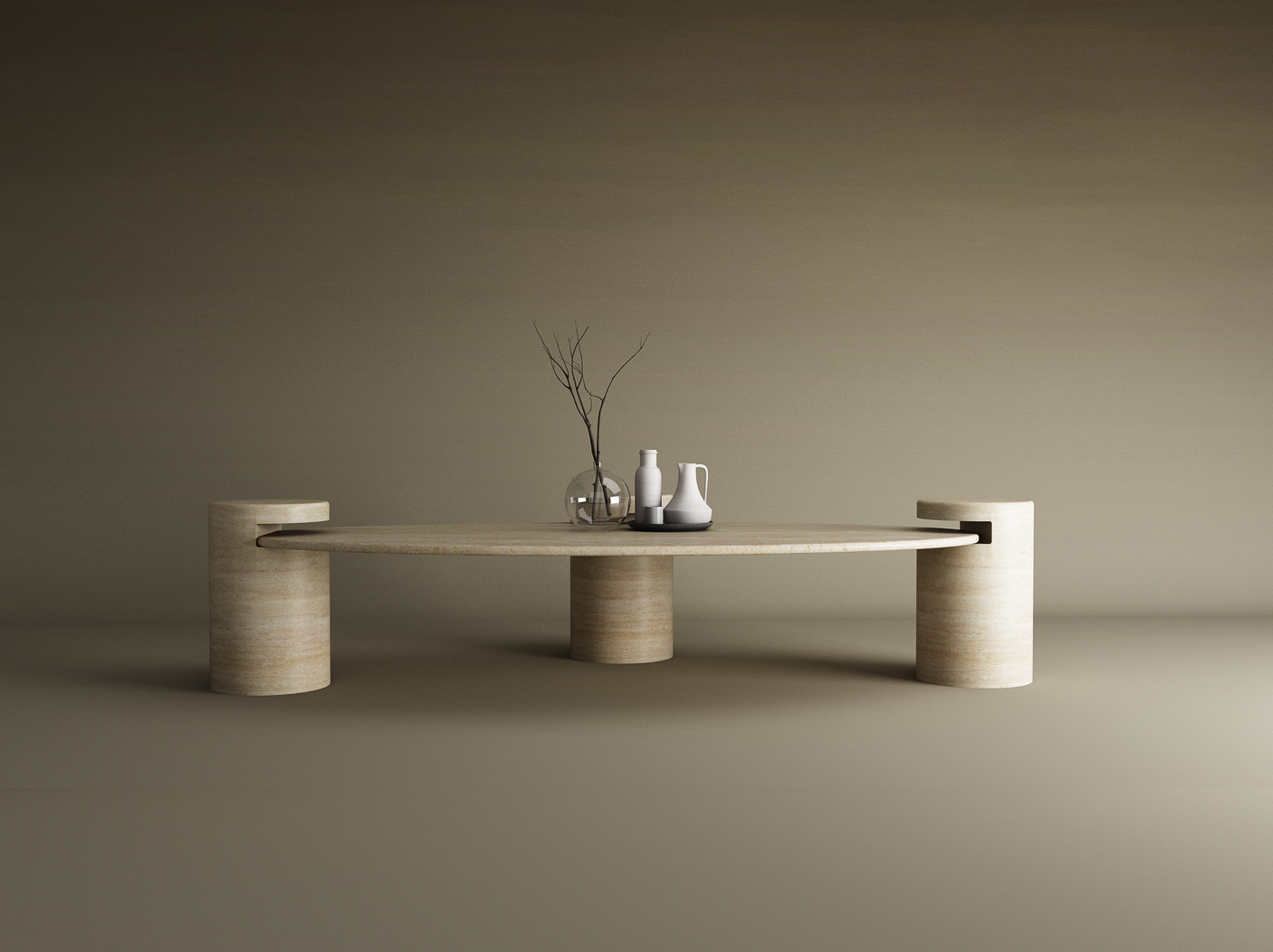 The TRAVERTABLE Ellipse Travertine Coffee Table with Cylindrical Base sits in a neutral room, topped with two vases, a white pitcher, and bare twigs for a simple, modern look against a plain backdrop.