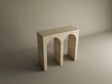 The TRAVERTABLE Travertine Console Table features a solid stone build and two arch-shaped legs, creating a customizable statement piece that showcases minimalist geometric design in a softly lit, neutral space.