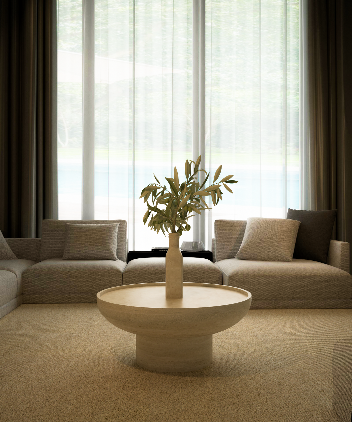 A modern living room features a beige sectional sofa, gray cushions, and the TRAVERTABLE Round Travertine Coffee Table with a solid cylindrical base. Sheer curtains cover floor-to-ceiling windows, highlighting minimalist style.