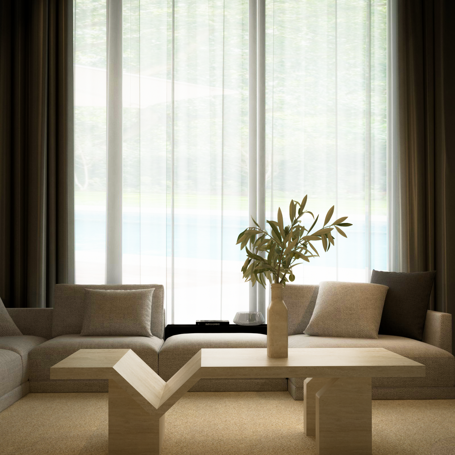 A modern living room features a beige sectional, a TRAVERTABLE Architectural Travertine Coffee Table with Sculptural Base, and a tan vase with green branches. Sheer white curtains and brown drapes on floor-to-ceiling windows fill the space with natural light.