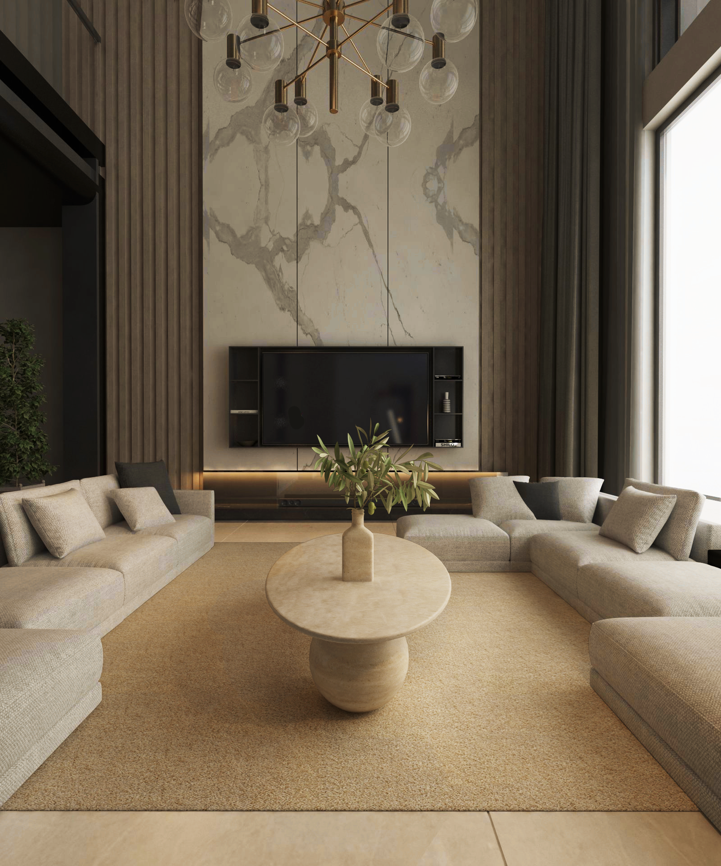 A modern living room with neutral tones features two beige sectionals around the TRAVERTABLE Ellipse Travertine Coffee Table with Stone Ball Base. A marble accent wall hosts a large TV, while tall windows and a gold chandelier brighten the space.