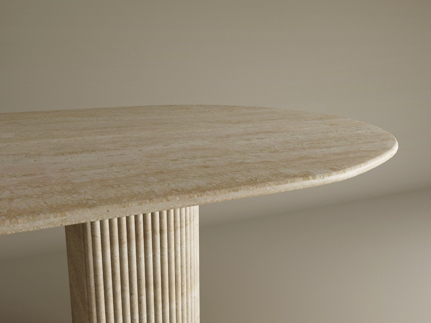 A close-up of the TRAVERTABLE Oval Travertine Dining Table reveals its natural travertine stone top with rounded edge and fluted solid base, set against a plain beige background. The table is customizable to fit any dining space.