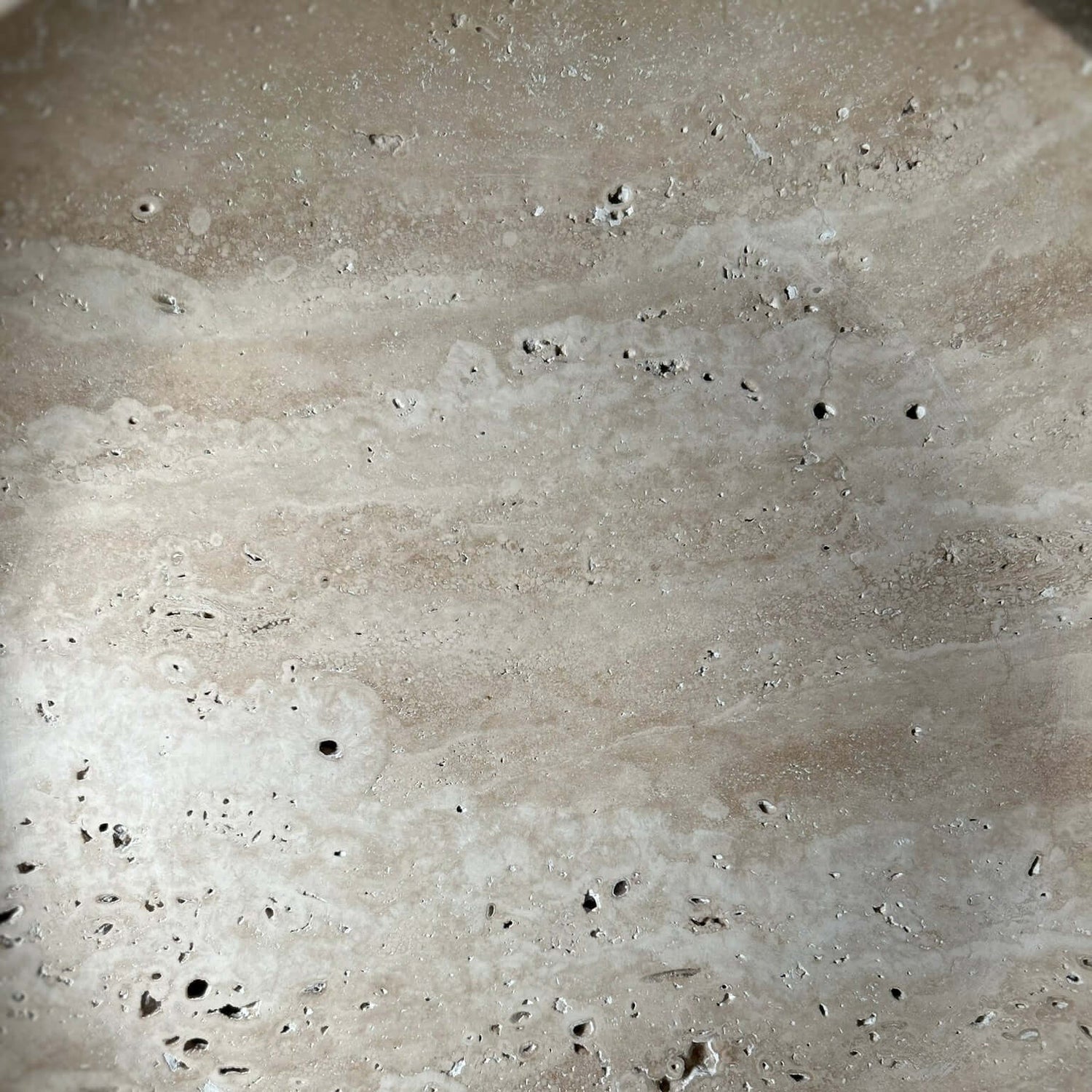 The Timeless Travertine Artisanal Bowl by Travertable features a textured beige surface with scattered small holes and speckles, reminiscent of natural travertine. Its subtle color and texture variations showcase natural artistry, offering an earthy and rustic ambiance.