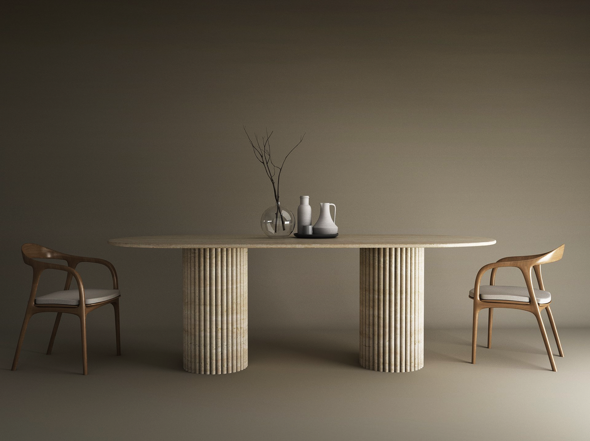 The TRAVERTABLE Oval Travertine Dining Table with Vertical Groove Base features a natural stone top, organic base, and is paired with two wooden chairs with white cushions. Minimalist decor includes a glass vase and ceramic pitchers against a beige background.