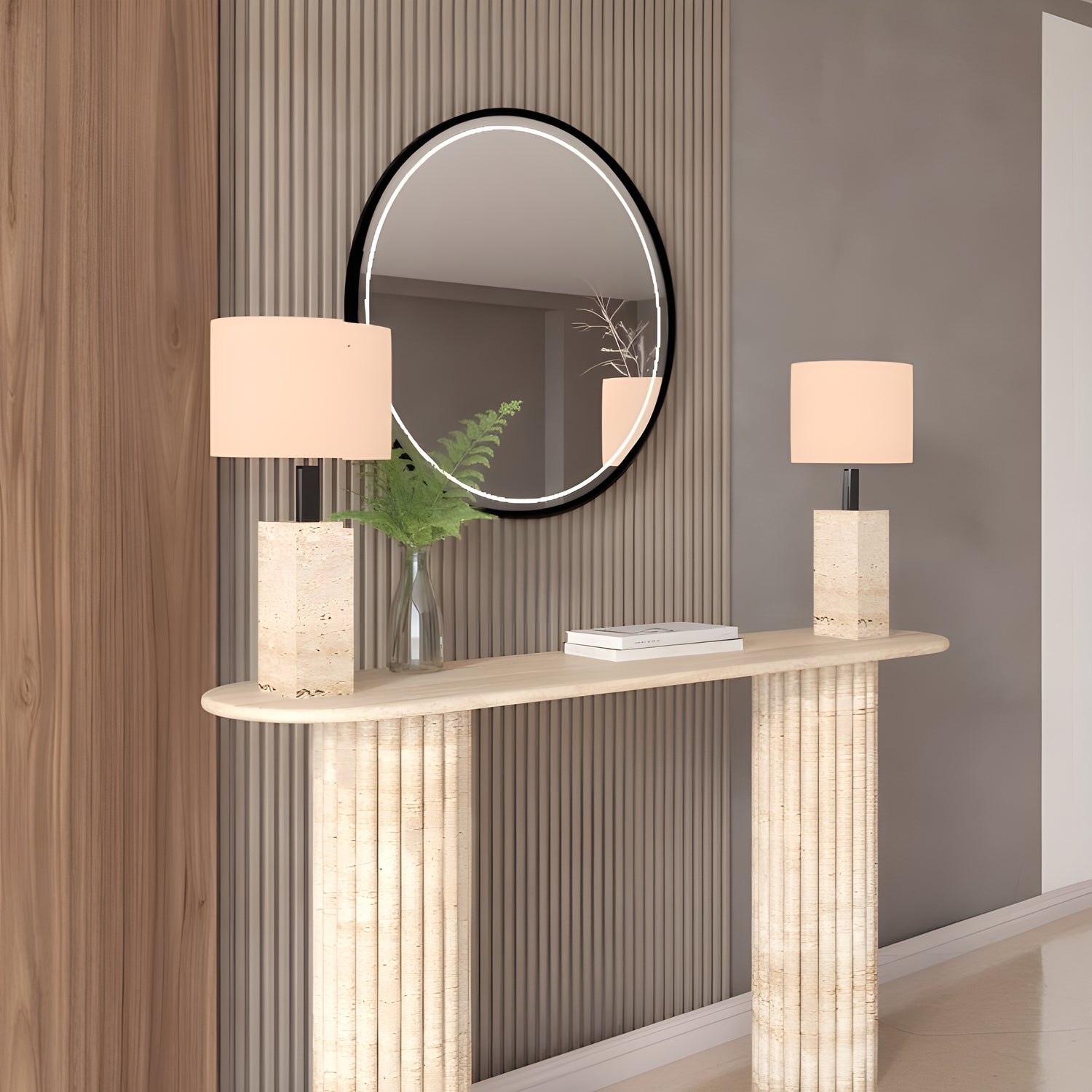 The Ovale Travertine Console Table with a vertical groove organic stone base by TRAVERTABLE is styled against a grooved wall, topped with two matching lamps and a vase of green foliage, while a round mirror above reflects the room.