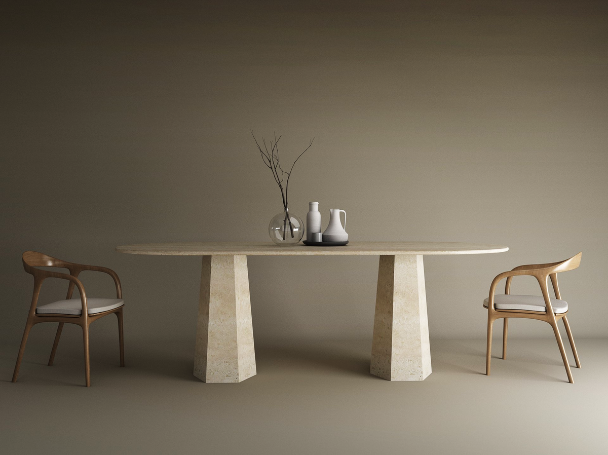 A minimalist dining setup features the TRAVERTABLE Oval Travertine Dining Table with Tapered Round Base, two wooden chairs with white cushions, a vase with dried branches, and two pitchers, all set against a plain beige background.