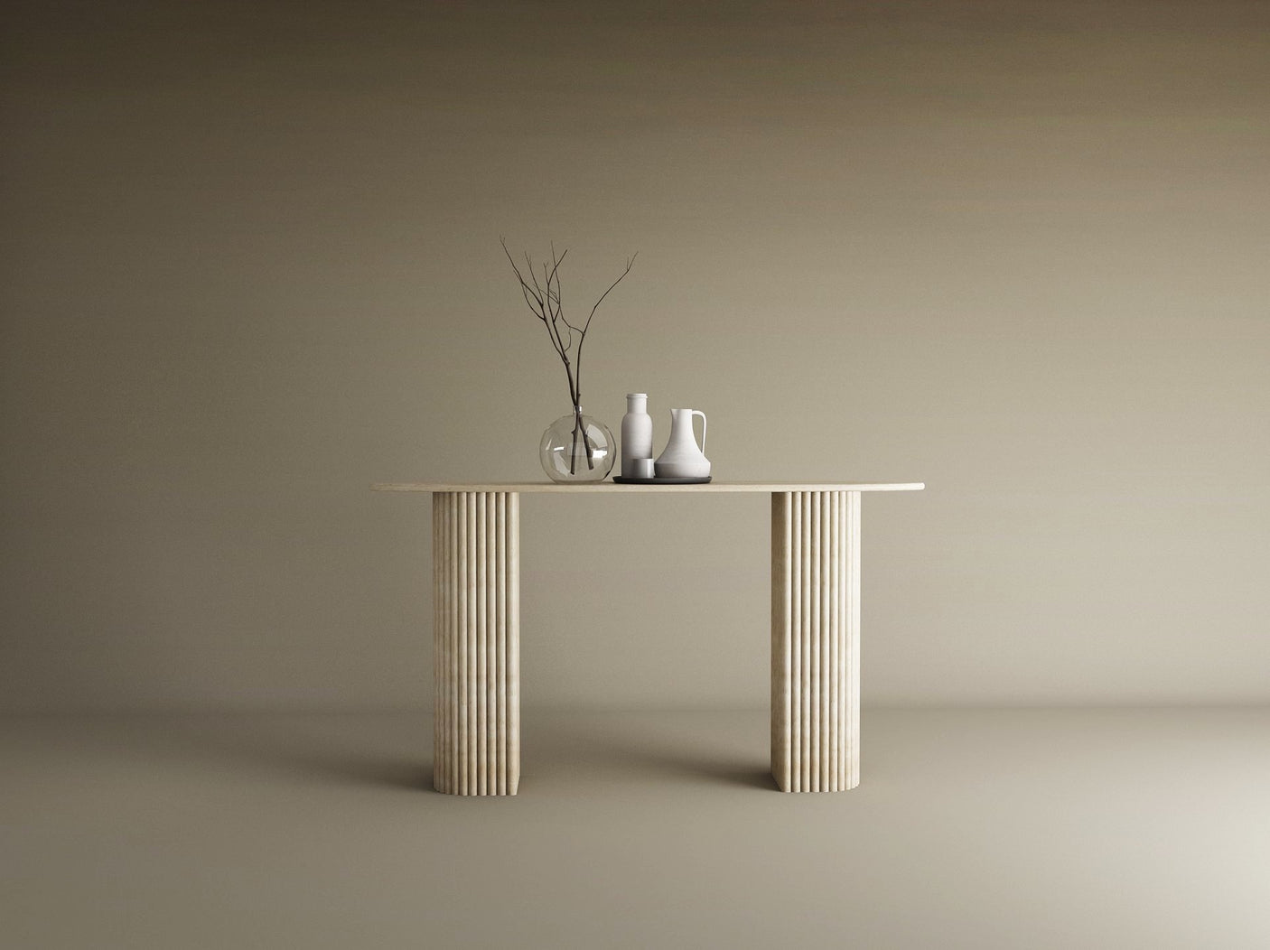 Against a plain beige backdrop, the TRAVERTABLE Ellips Travertine Console Table with Fluted Round Base displays refined luxury, adorned with two white ceramic pitchers and a clear glass vase of bare branches.