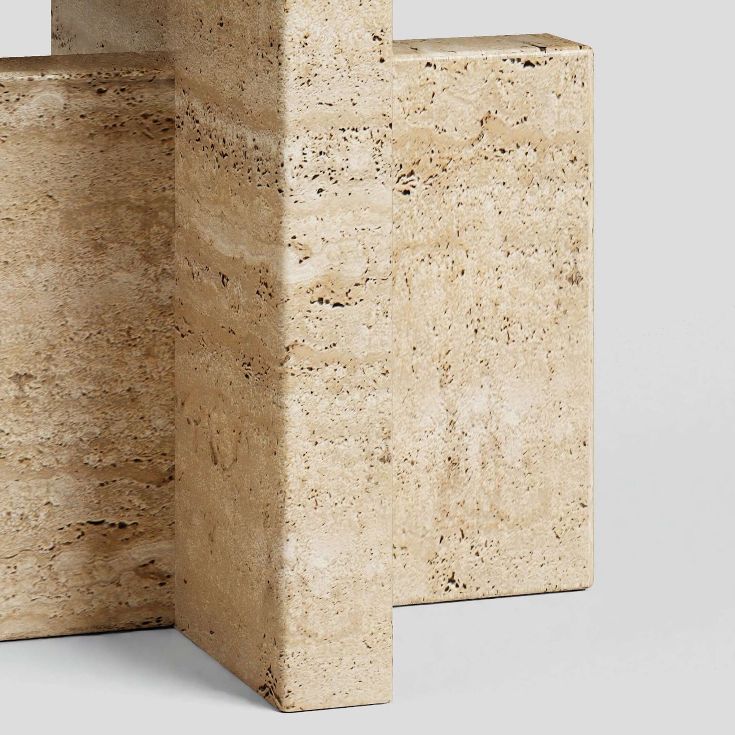 Close-up of intersecting rectangular blocks crafted from textured honed travertine stone with natural speckles and lines. The sleek, geometric form evokes a modern, minimalist aesthetic, ideal for Travertables Travertine Scepter Side Table in any contemporary space.
