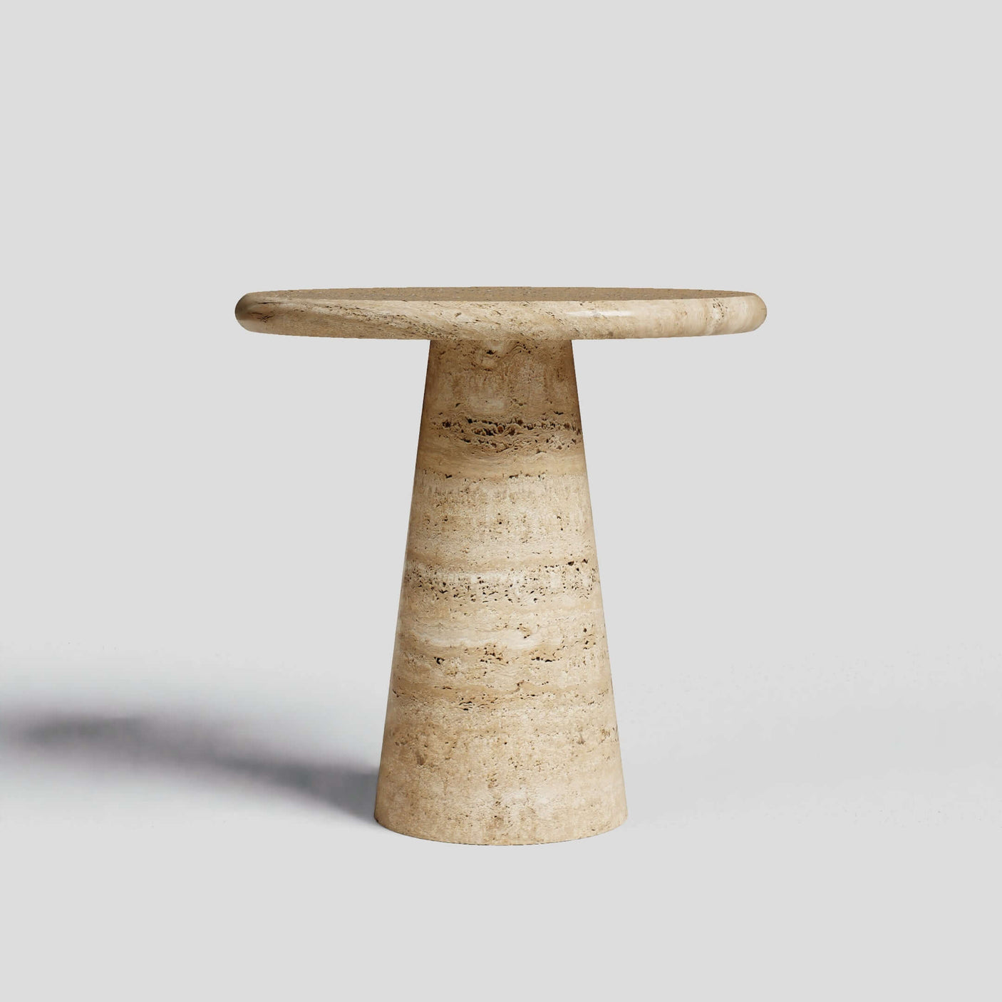 Set against a plain gray background, the Tavolino Pietra Travertine Column Table by Travertable showcases a classic European-inspired design with a round top and conical base, handcrafted from natural stone.