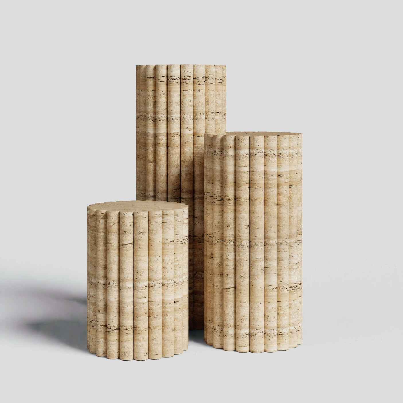 The Travertable Travertine Elegance Pillar Trio features three sculptural pedestals of varying heights, each with a vertical fluted texture, resembling classical columns, set against a light gray background.