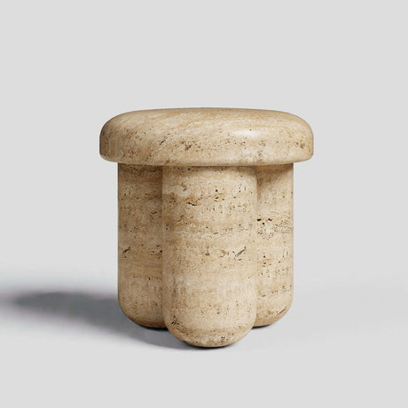 The Travertable Travertine Elegance Accent Table showcases a natural stone finish with a smooth round top and three rounded, pillar-like legs, resembling light-colored travertine. It is set against a plain light gray background.