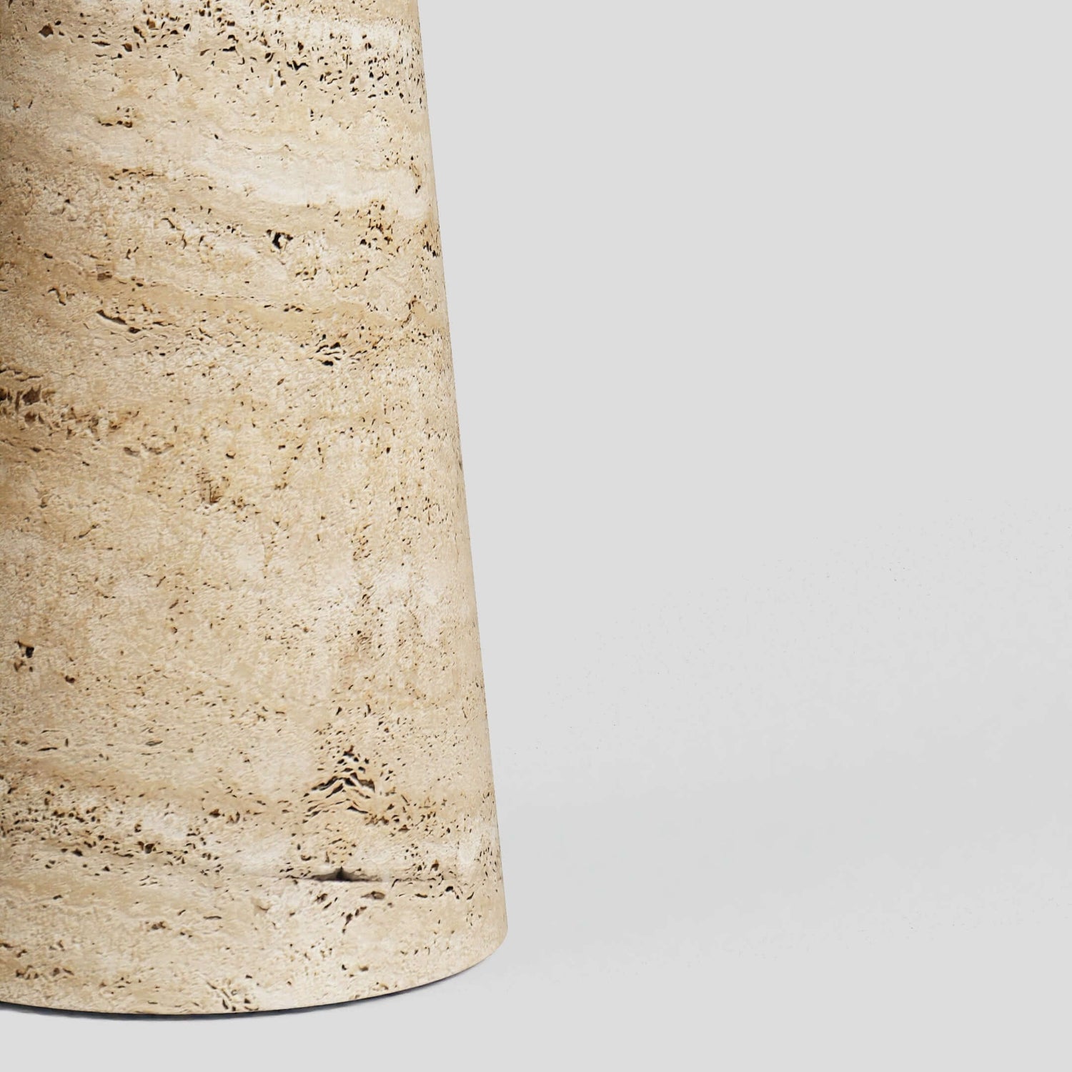 Close-up of Travertables Tavolino Pietra Travertine Column Table, a handcrafted cylindrical stone design with natural streaks and patterns, set against a plain gray background.