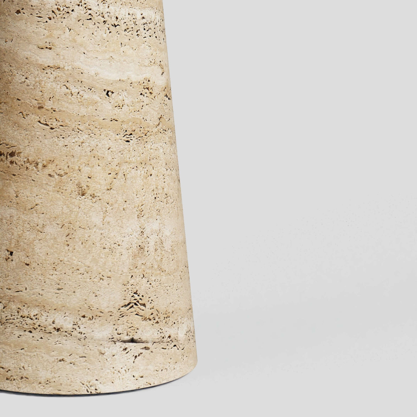 Close-up of Travertables Tavolino Pietra Travertine Column Table, a handcrafted cylindrical stone design with natural streaks and patterns, set against a plain gray background.