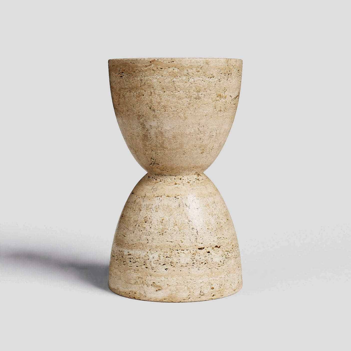 The Eda Beige Travertine Sphere Table by Travertable is a minimalist stone hourglass stool with a smooth, textured beige surface. Its two rounded halves elegantly meet at the center against a light gray background, capturing the essence of travertine table design.