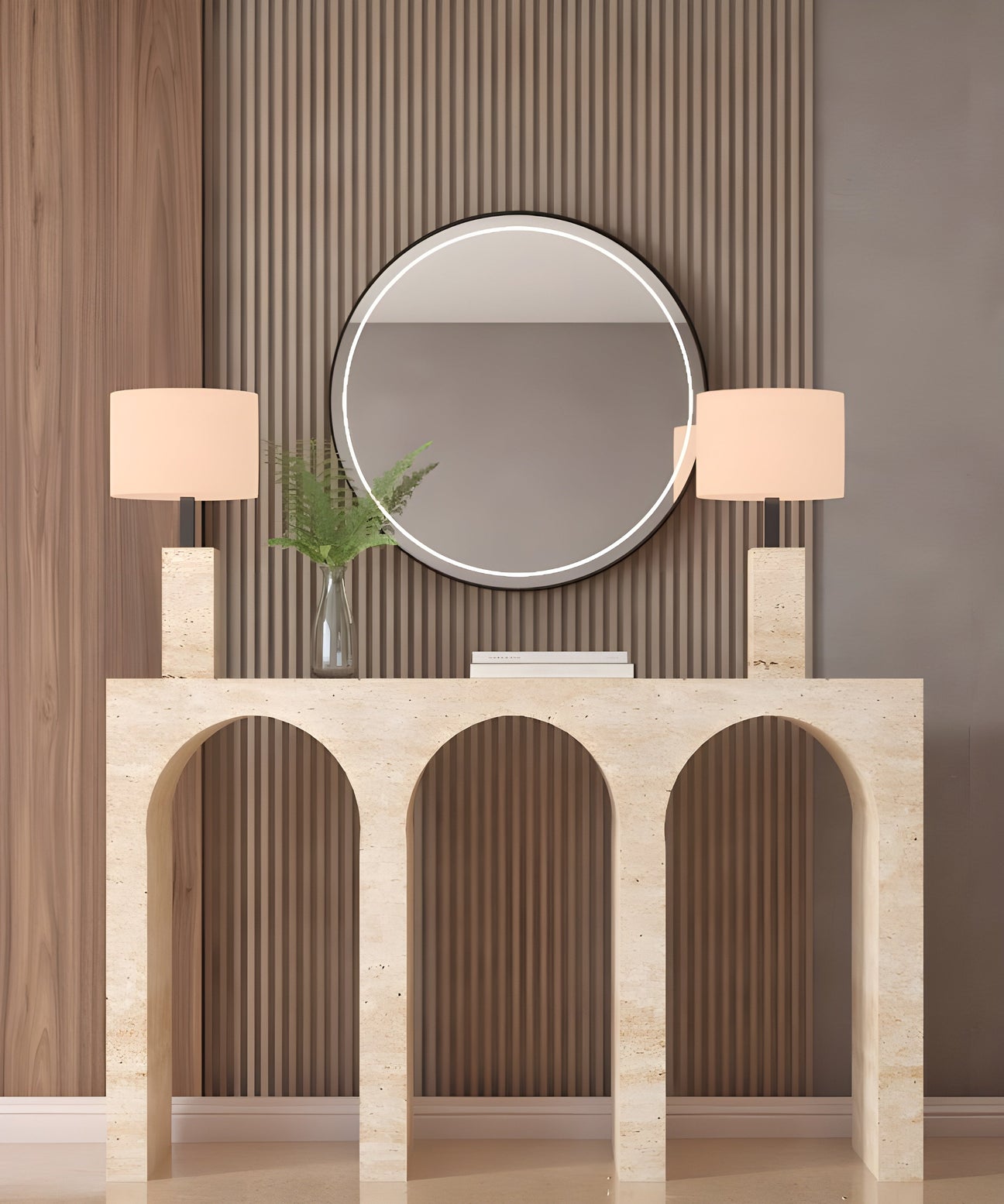 A modern entryway with a beige stone console table featuring three arches, two matching lamps with beige shades, a glass vase with green fern leaves, books, and a round mirror on the wall.