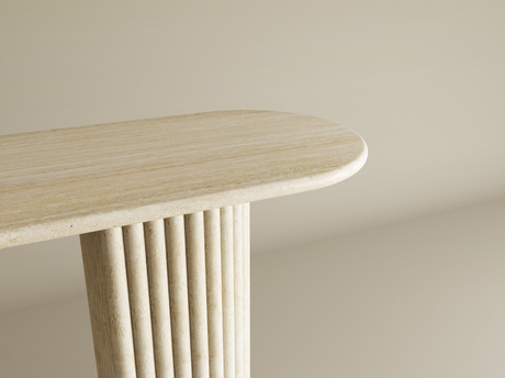 A close-up of a light-colored, oval-shaped tabletop with vertical fluted legs against a plain beige background. The design appears minimalist and modern.