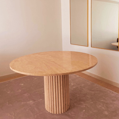 The Classic Round Travertine Dining Table by Travertable, featuring a textured cylindrical base, stands on a light brown rug in this minimalist room. The white walls and large mirror reflect the bespoke piece and the elegant wall decor.