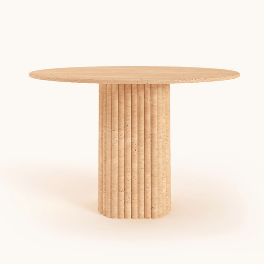 The Harmony Oval Travertine Dining Table by Travertable features a round, beige, modern travertine design with a smooth wooden top and vertical fluted cylindrical base against a plain background.