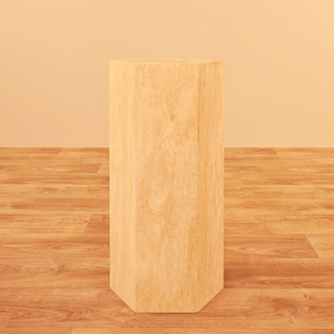 The Geometric Travertine Pedestal by Travertable, featuring a unique sculptural design and architectural appeal, stands tall like a hexagonal column on a matching wooden floor against a beige background.