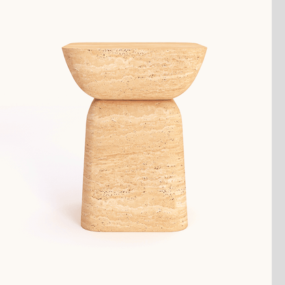 The Modern Minimalist Travertine Side Table by Travertable is a tan, textured stone accent with a bowl-shaped seat and trapezoidal base, placed against a plain, light background.