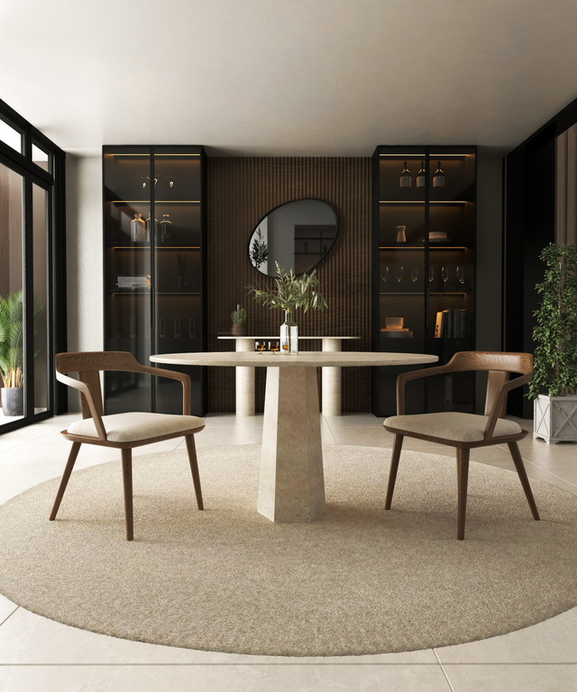 A modern dining room features the TRAVERTABLE Oval Travertine Dining Table with Rockcone Center Base, two wooden chairs, a circular rug, built-in glass cabinets, a round mirror, and decorative items on a wood-paneled wall.