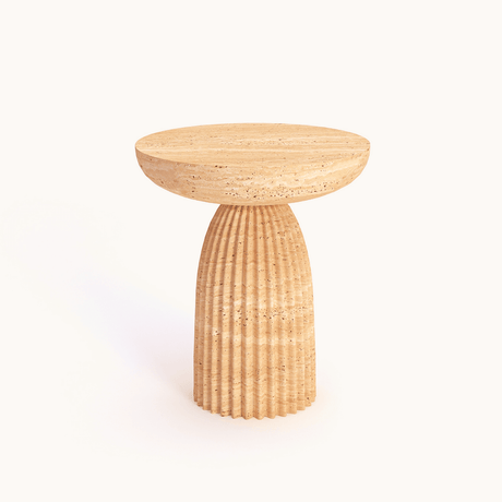 A round side table by Travertable features a textured fluted base and a smooth top, mirroring elegant travertine. Called the Fluted Travertine Side Table, its a hand-carved natural stone accent with a sculptural column base against a plain background.