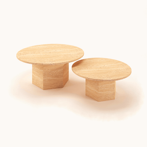 Set against a plain backdrop, two wooden tables showcase a timeless design with round tops and sturdy rectangle bases. The elegance of the Desert Serenity Travertine Coffee Table by Travertable is highlighted as the smaller piece sits gracefully in front of its larger counterpart.