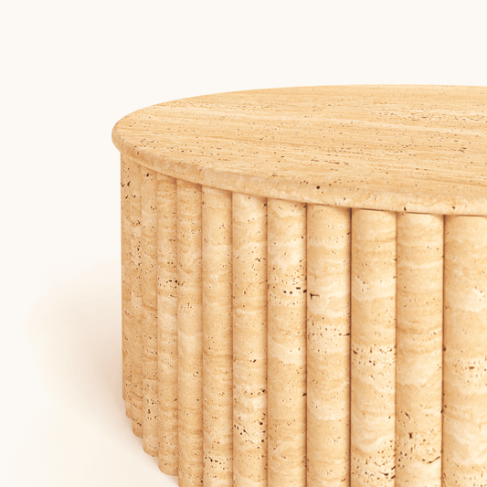 The Alpine Oasis Travertine Coffee Table by Travertable, handcrafted from solid travertine, features a round beige design with a ribbed cylindrical base and flat top. Its smooth, natural stone texture with subtle variations complements elegant interiors beautifully.