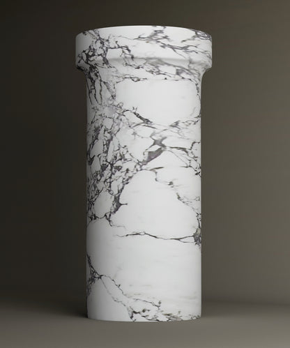 The TRAVERTABLE Calacatta Marble Pedestal Vanity Sink features a tall, cylindrical design with a wider top and elegant gray veining. The plain backdrop accentuates its timeless, sophisticated look.