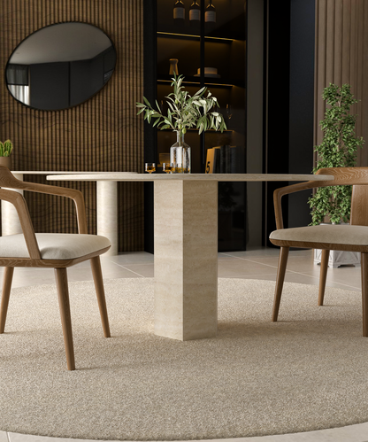 The TRAVERTABLE Oval Travertine Dining Table features a geometric hexagonal base and beige stone top, paired with two wooden chairs with beige cushions on a light rug, creating a modern look with timeless elegance in this neutral-toned room.