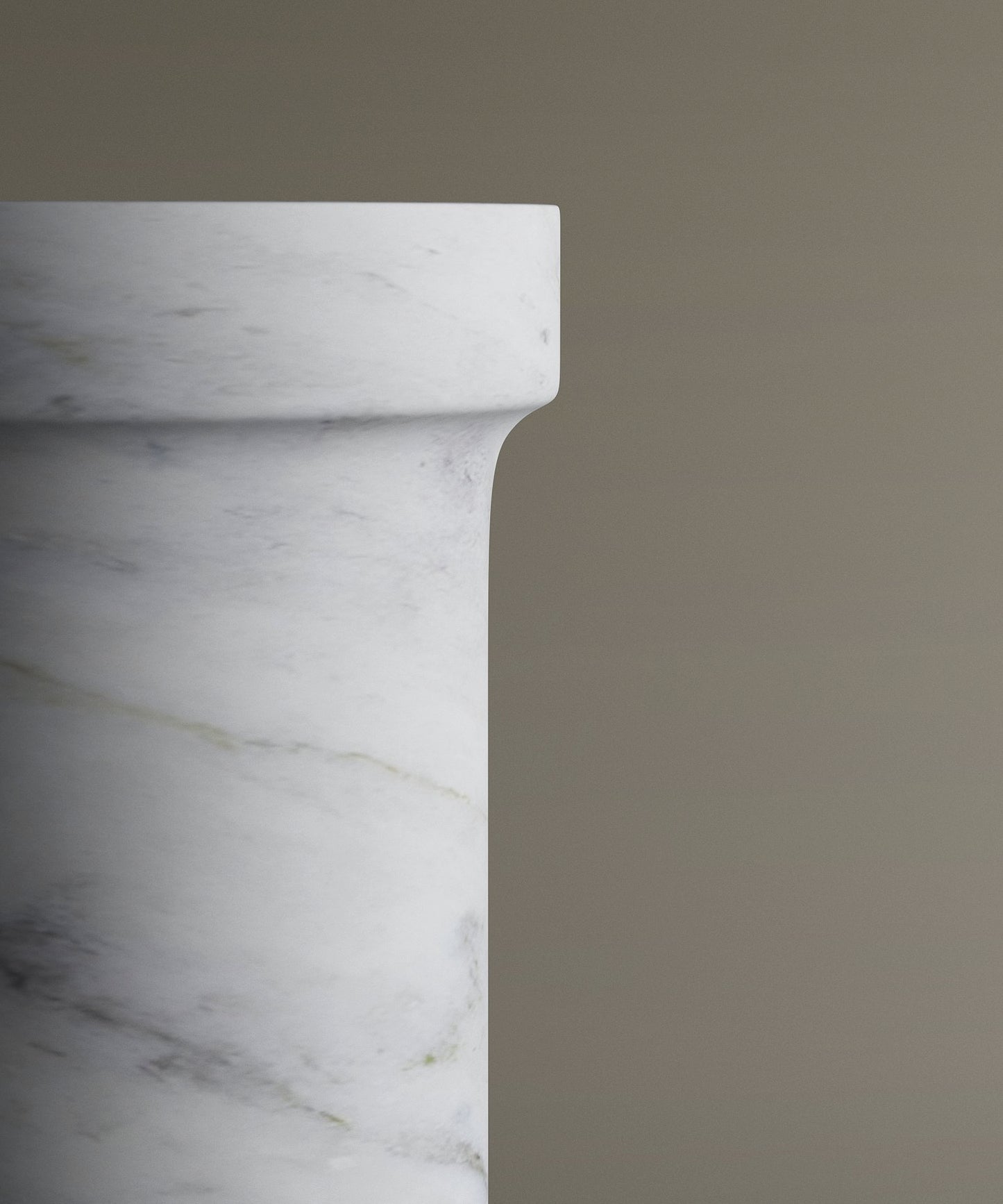 A close-up of the upper edge of the TRAVERTABLE Carrara Marble Pedestal Vanity Sink highlights its soft gray veining and polished surface, set against a plain light brown background—ideal for refined interiors.
