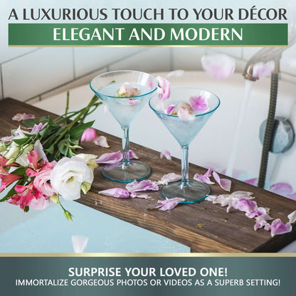 Two elegant, BPA-free large martini glasses by Mamaco Home sit on the edge of a bathtub, accompanied by a bouquet of pink and white flowers. Overlay text highlights their modern luxury and invites photo or video capturing in this unique setting.