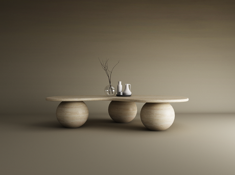 The TRAVERTABLE Wavy Travertine Coffee Table features an irregular oval top and three stone ball bases. Styled with a glass vase, branch, and ceramic pitchers on a tray, it sits against a seamless gradient of neutral beige tones.