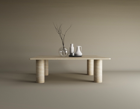 The TRAVERTABLE Square Travertine Coffee Table with a solid cylindrical base displays a glass vase with bare branches, a white ceramic pitcher, and a ceramic bottle, set against a plain beige background.